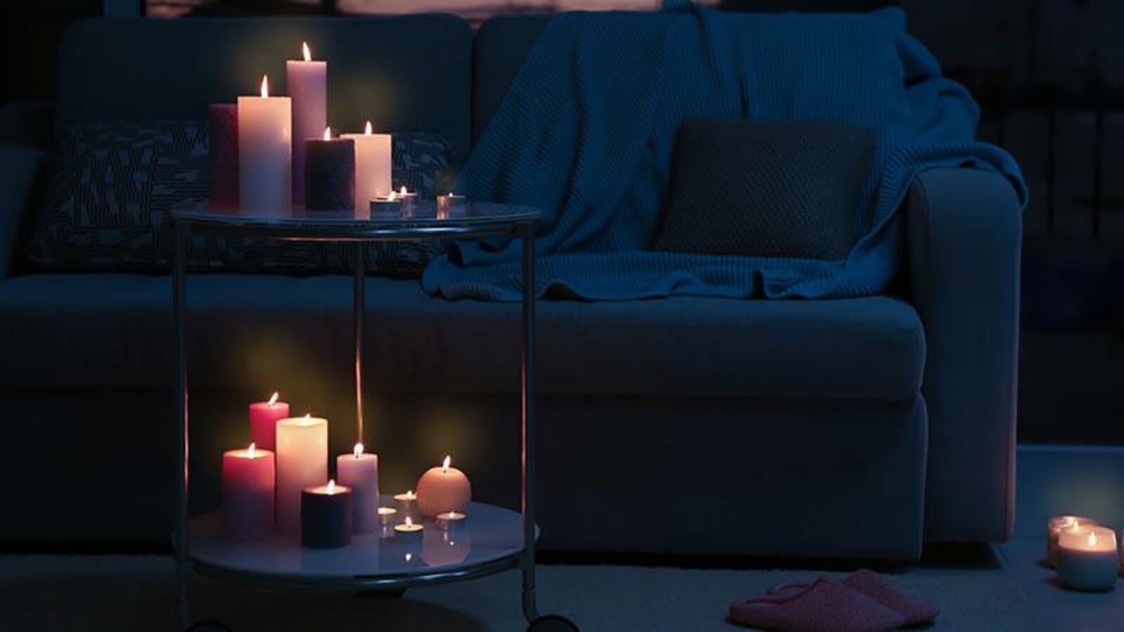 Multiple lit candles glowing on a side table in a dark, quiet living room