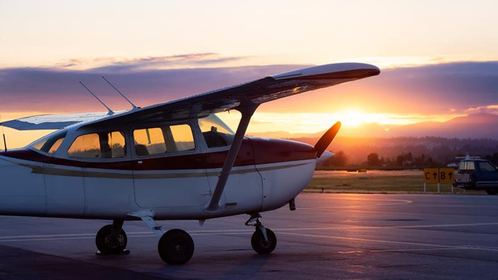 A small commercial propeller airplane parked on an airport tarmac at sunset