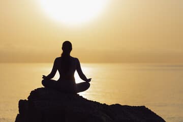 A silhouetted figure meditating against a sunrise window.