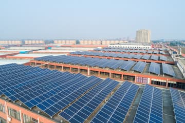 Aerial view of rows of solar panels covering the rooftops of an industrial complex