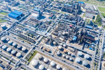 Aerial view of a mostly empty oil reserve tank complex on cracked dry ground.