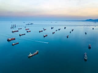 Aerial view of oil tankers queued at a narrow strait entrance.